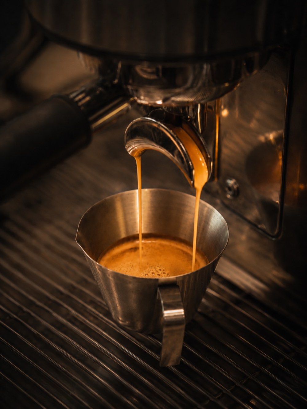 Espresso running from the portafilter into a steel pitcher.
