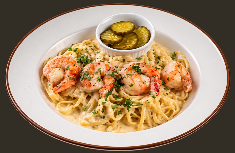 Fettuccine alfredo with shrimp in a cream sauce, scattered with parsley, pickles alongside.