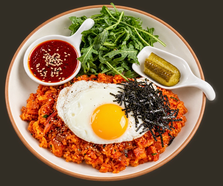 Kimchi fried rice under a sunny-side-up egg, with shredded nori, gochujang, arugula and pickles on the rim.