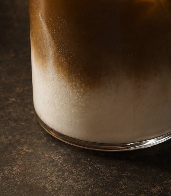 The base of an iced hojicha latte, roasted tea settling in a clean line over milk.