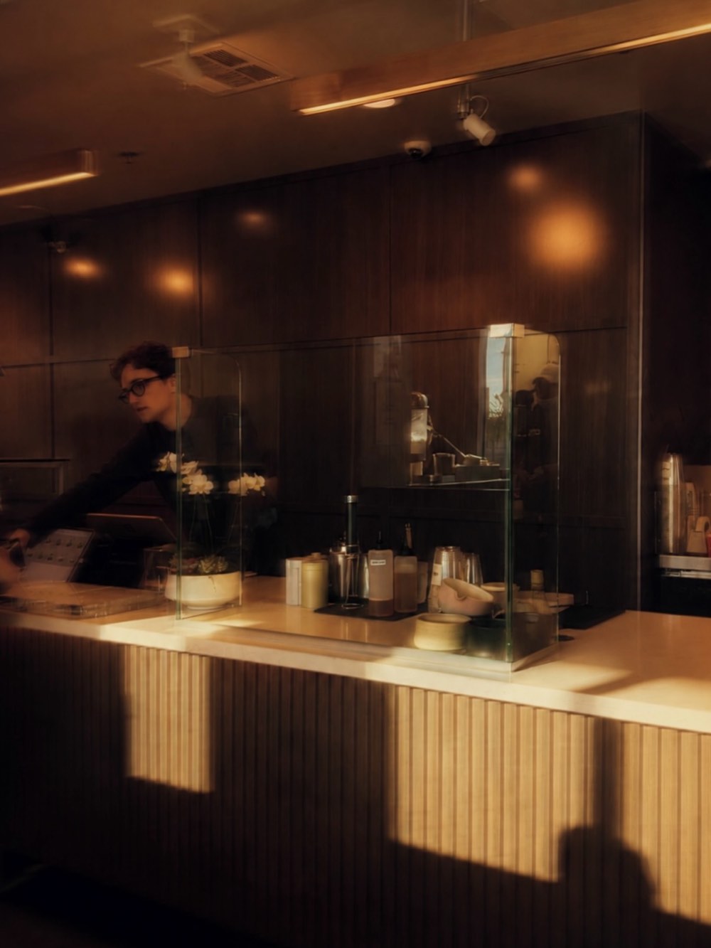 The counter in the evening, warm light over the fluted timber bar and pastry cases.