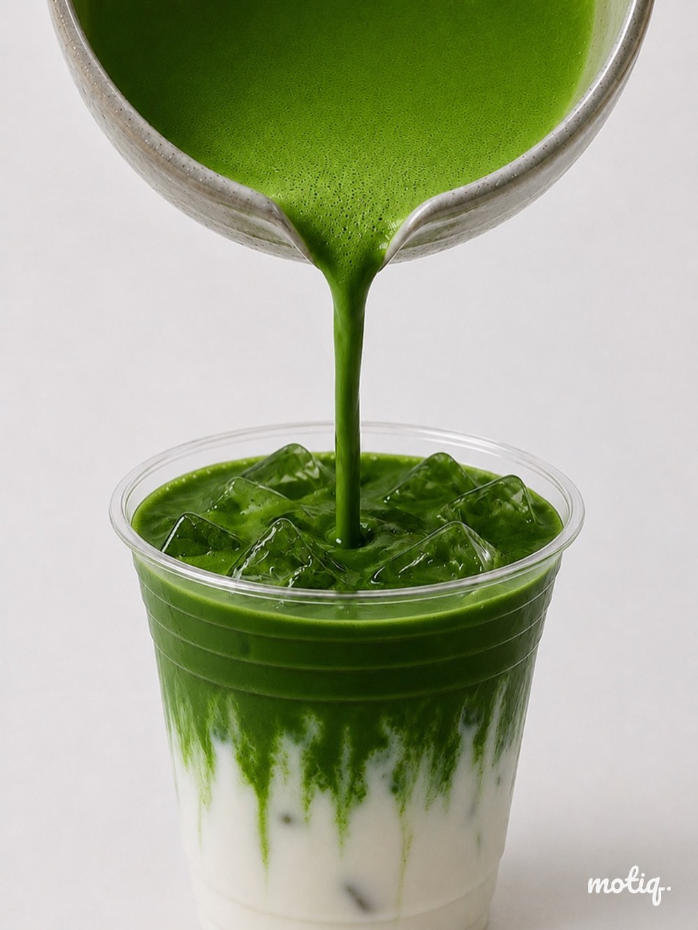Matcha poured from a stoneware pitcher into a Motiq cup of iced milk.