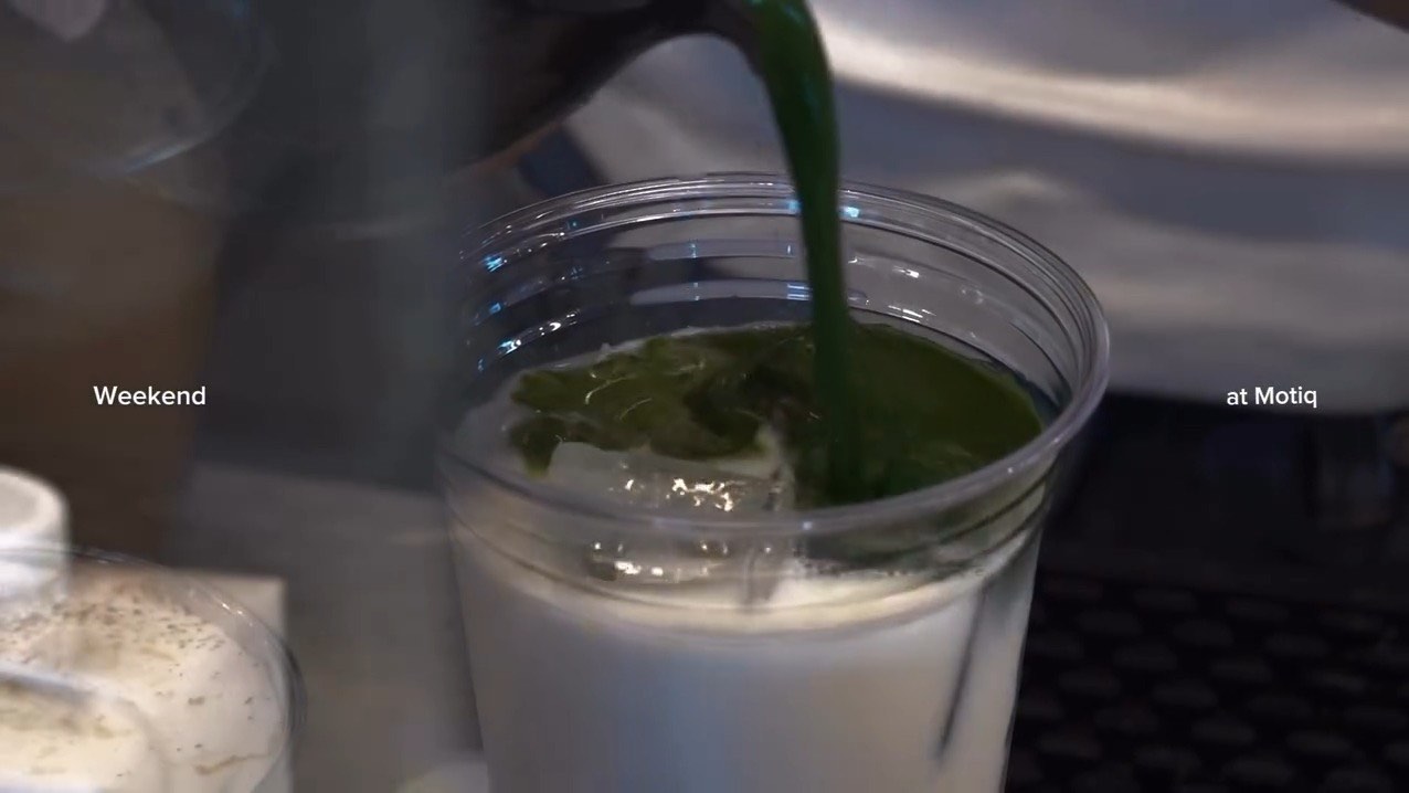 Matcha being poured from a pitcher into a cup of milk over ice at the Motiq bar.