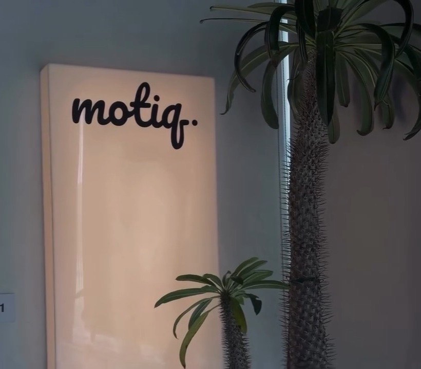The Motiq sign, a black script wordmark on a lit cream panel.